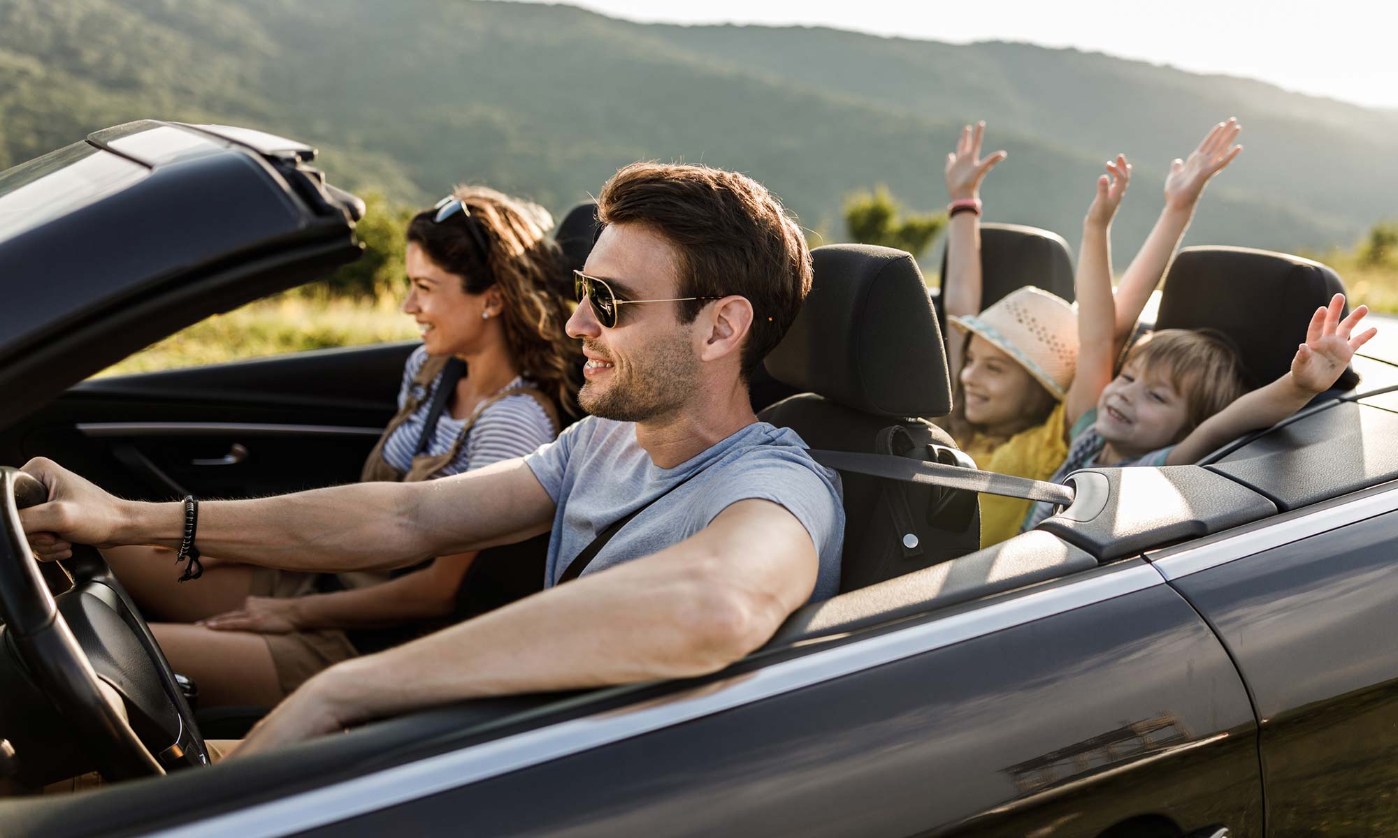 Una familia de cuatro personas conduciendo un descapotable por la carretera en un día soleado.