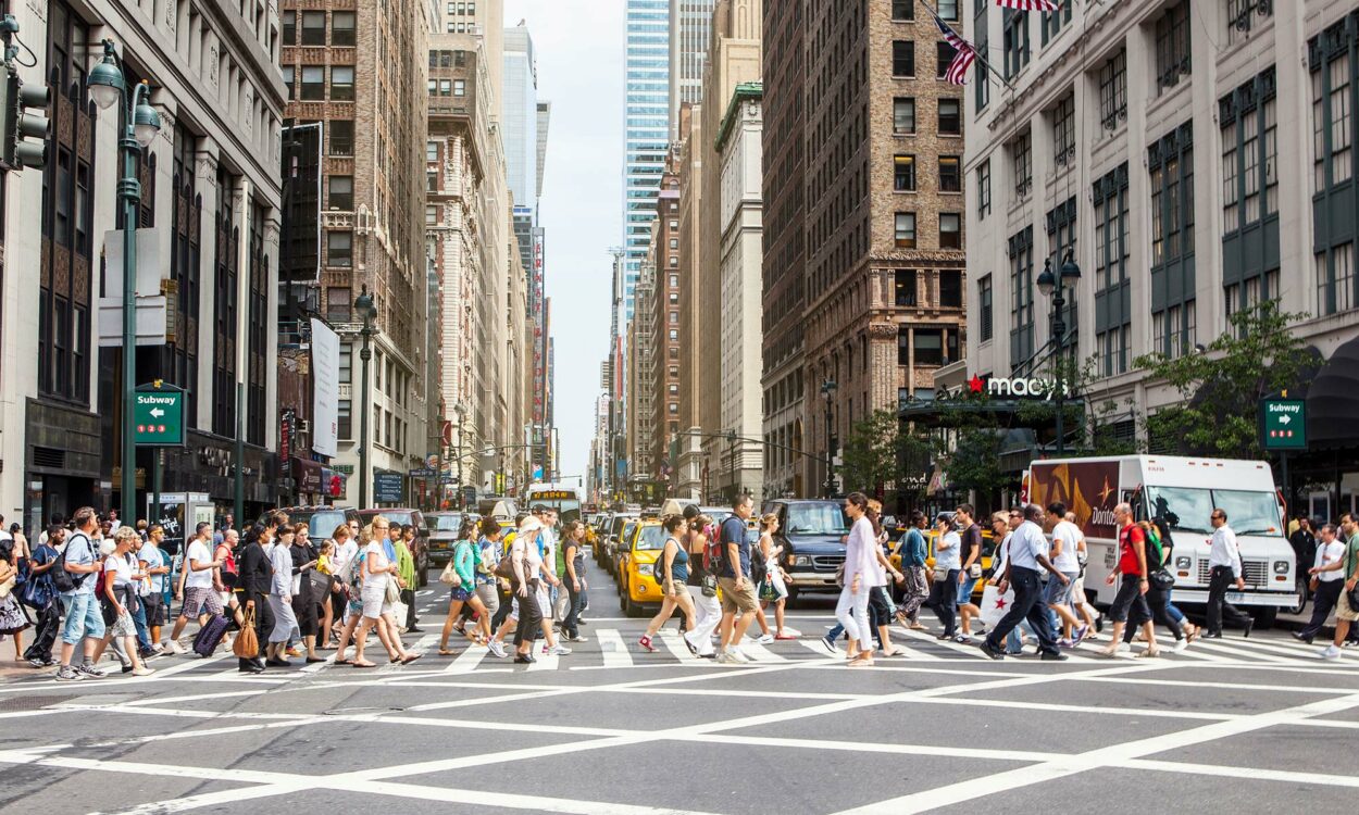 Un gran grupo de peatones cruzando frente a una fila de automóviles en un cruce peatonal de la ciudad de Nueva York.