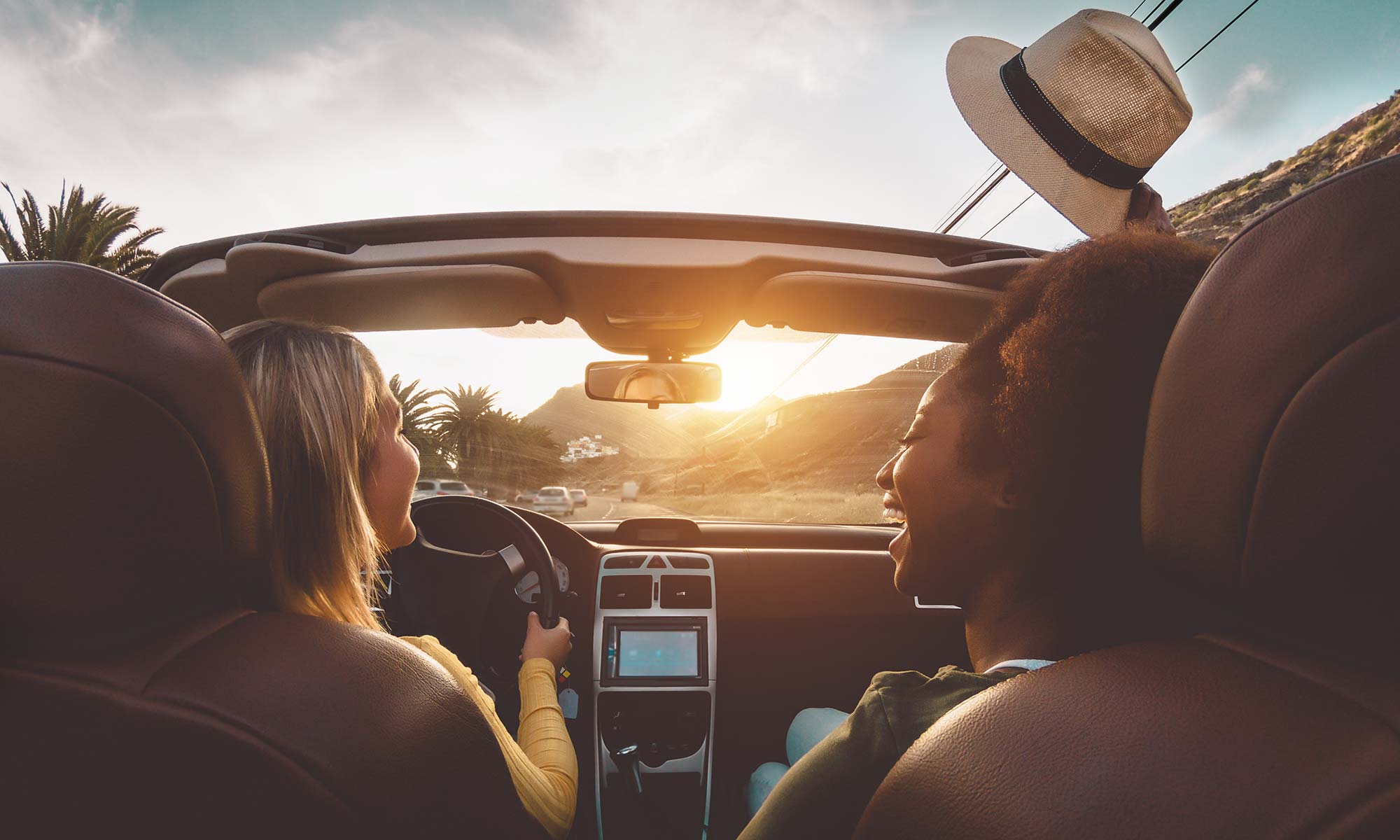 Dos amigas se divierten y ríen mientras conducen un descapotable al atardecer con la capota baja.