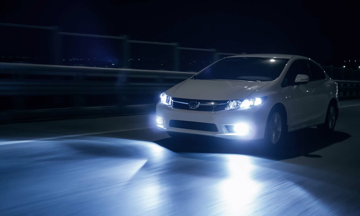 A vehicle driving down a road at night with the headlights on.