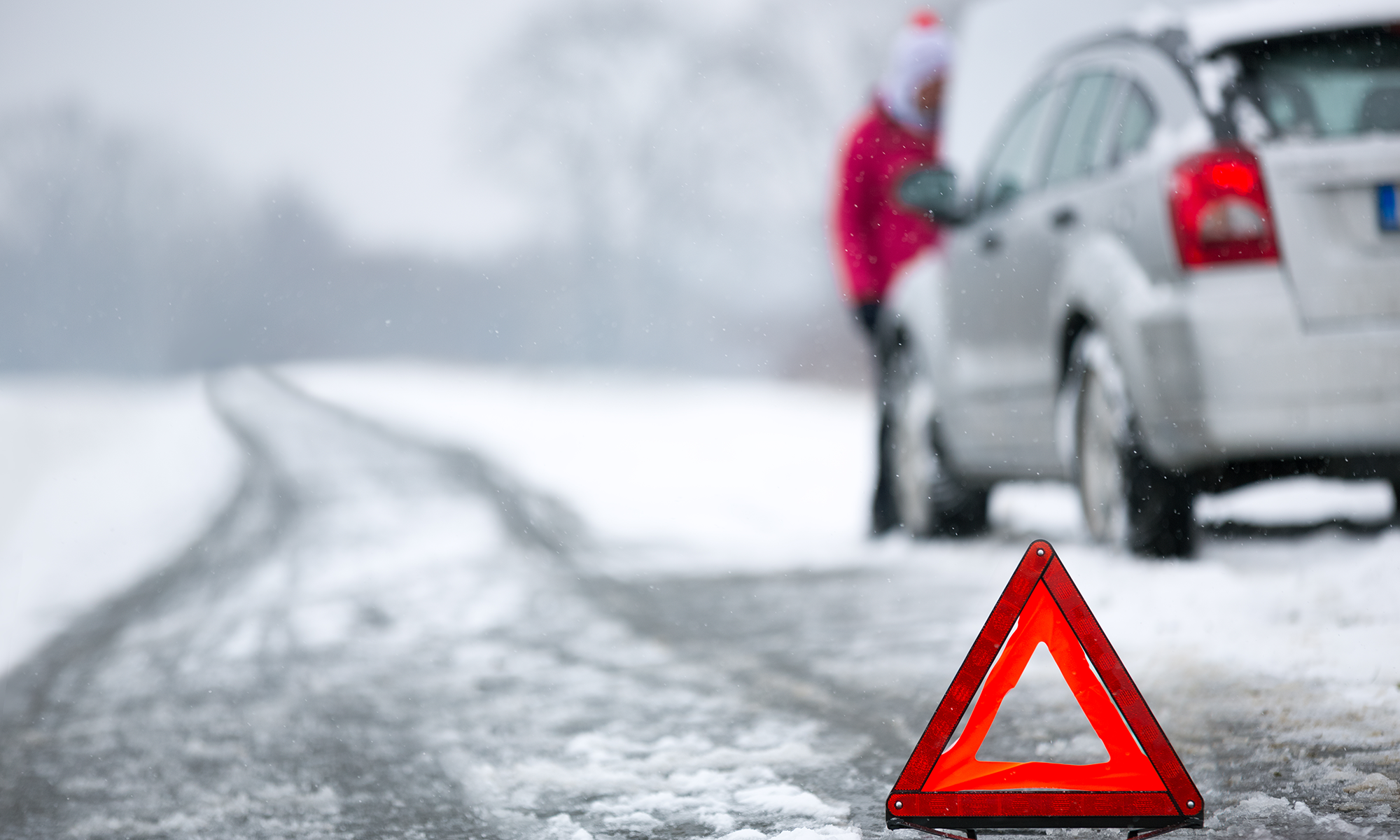 Un triángulo de emergencia vial colocado frente a un vehículo detenido en una carretera nevada.