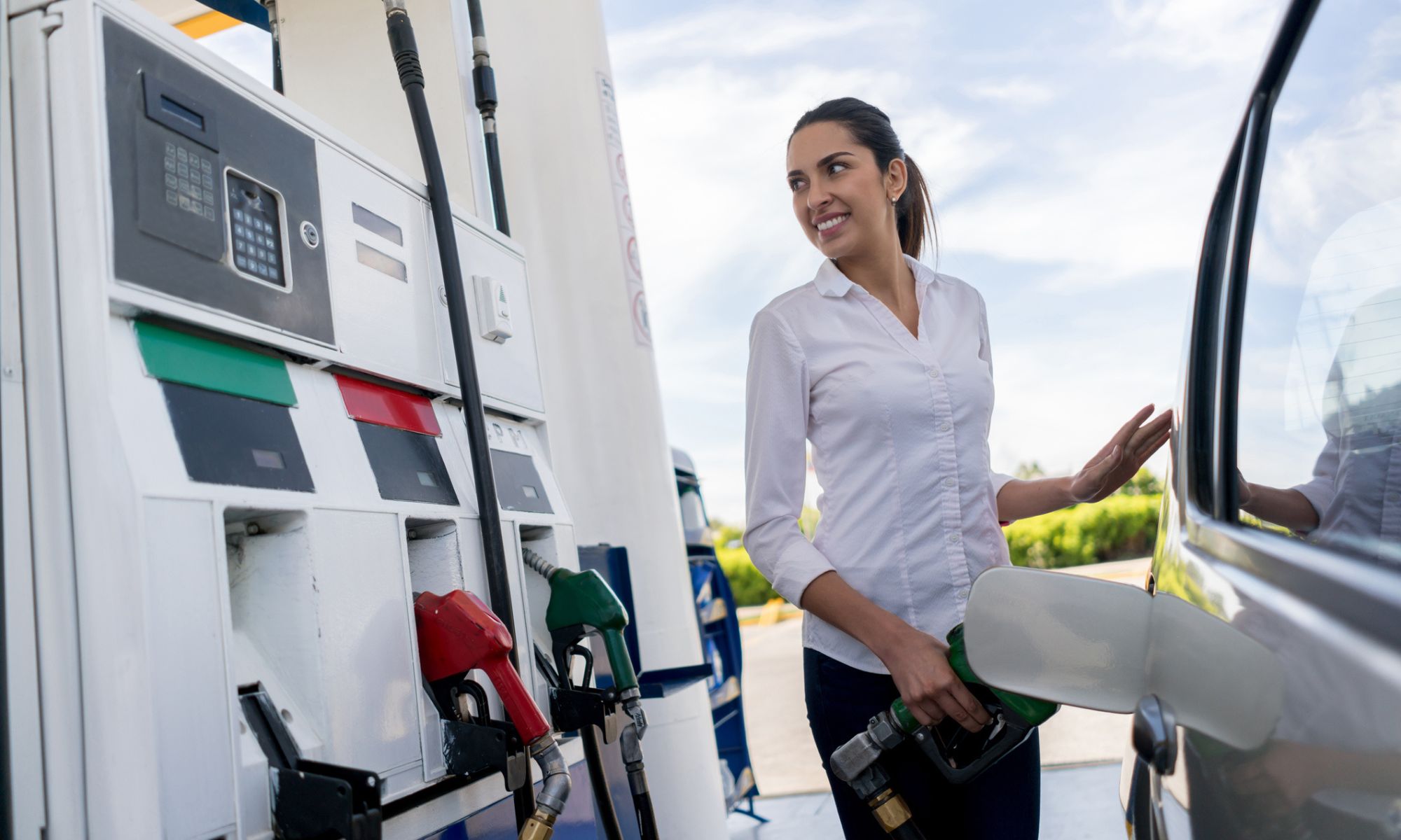 Mujer repostando su coche en una gasolinera y sosteniendo el surtidor de combustible