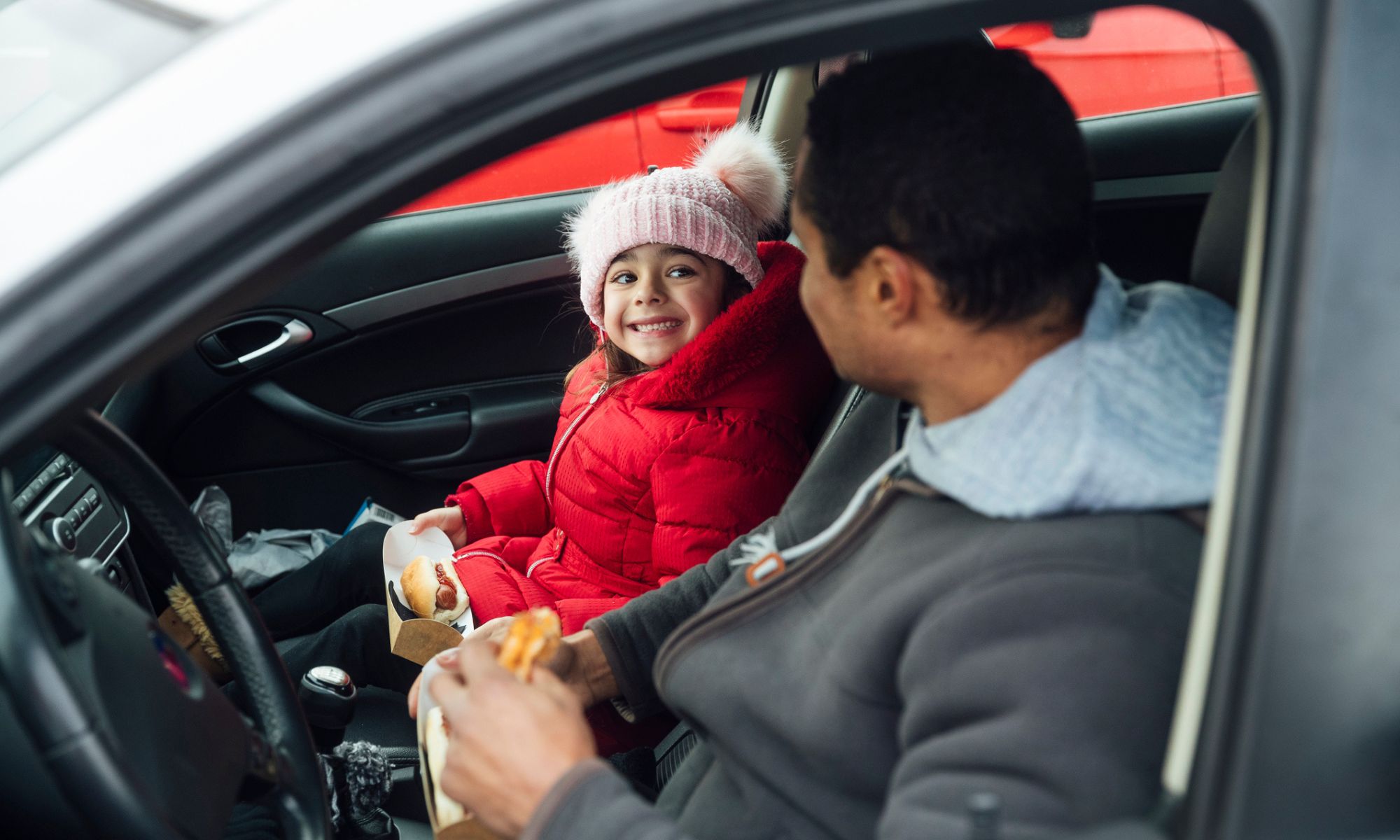 Padre e hija comiendo perritos calientes juntos sentados en su coche
