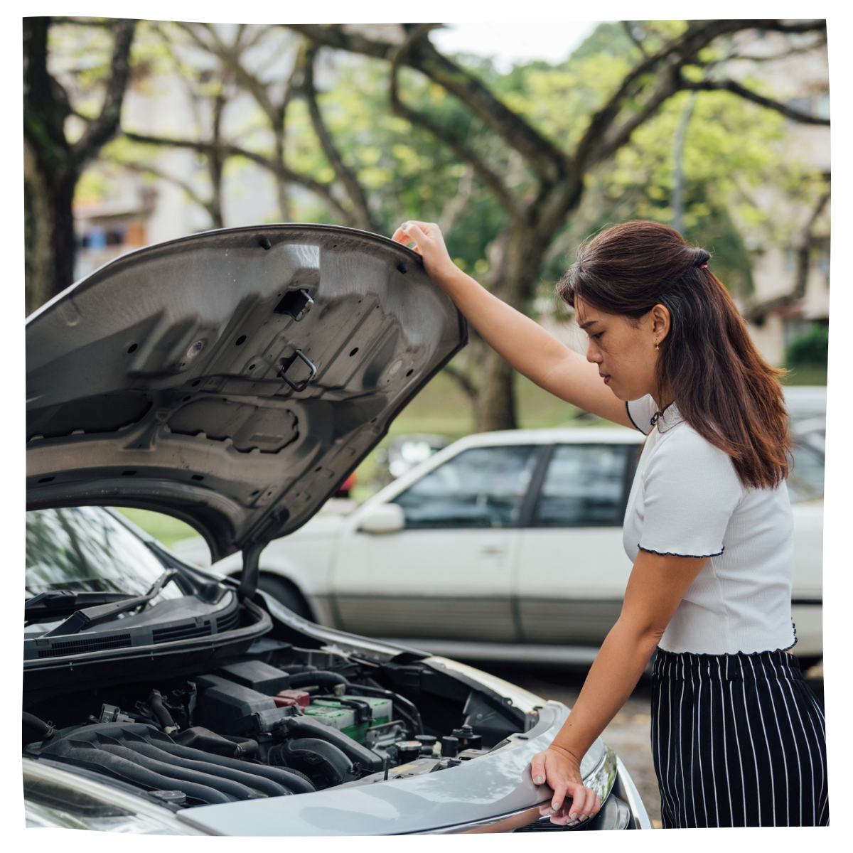 Woman driver looking at broken down car engine under hood on the street