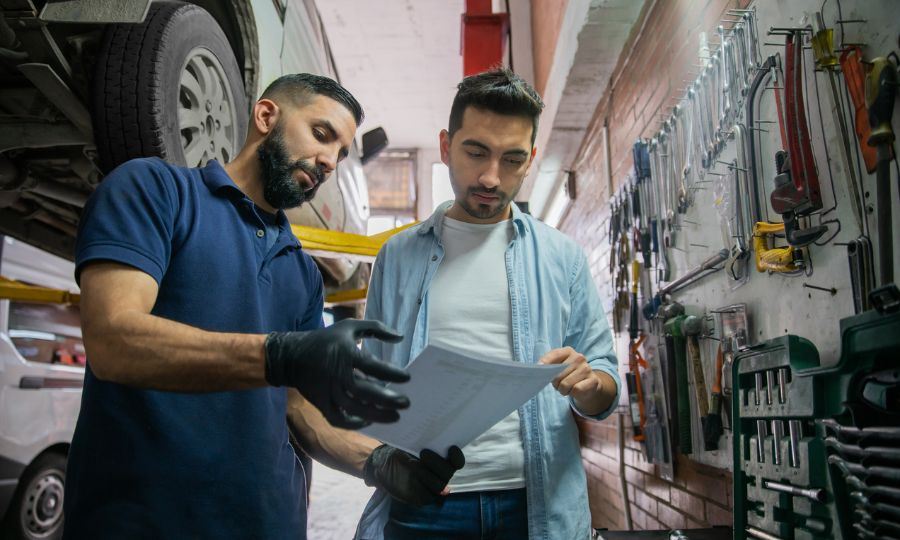 Male customer checking the list of the car parts changed at the auto repair shop with mechanic