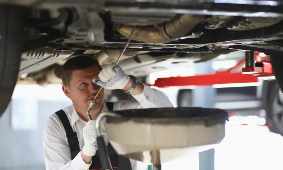 Mecánico de automóviles revisa el tren de rodaje del coche y la fuga de aceite