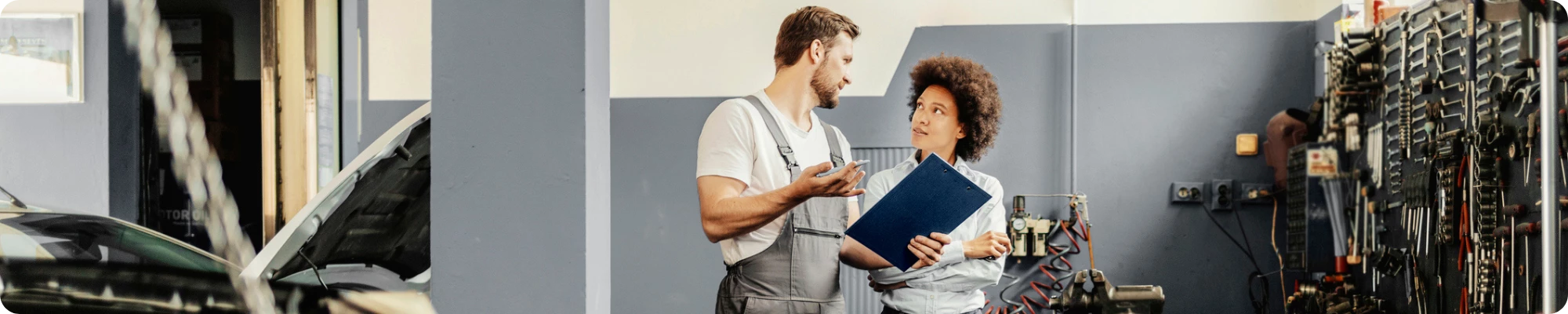 Male mechanic with a clipboard talking to a female customer
