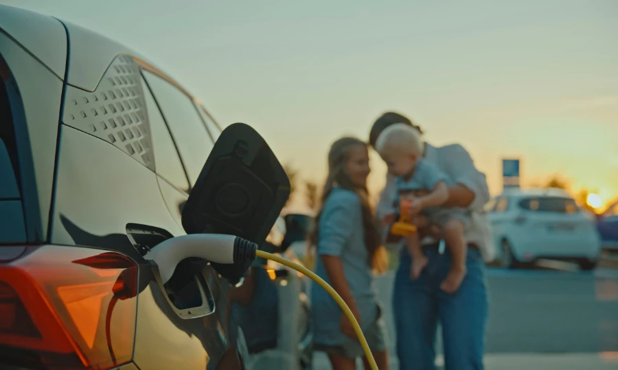 Mother with baby and young daughter stands near electric car charging station