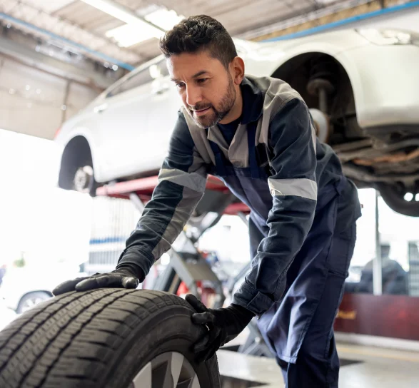 Male Mechanic Rolling Tire Away From Vehicle In Shop