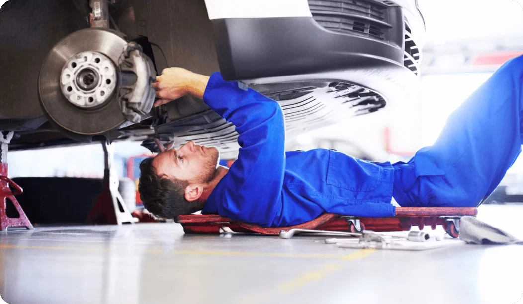 Male Mechanic In Blue Uniform Working Underneath White Car