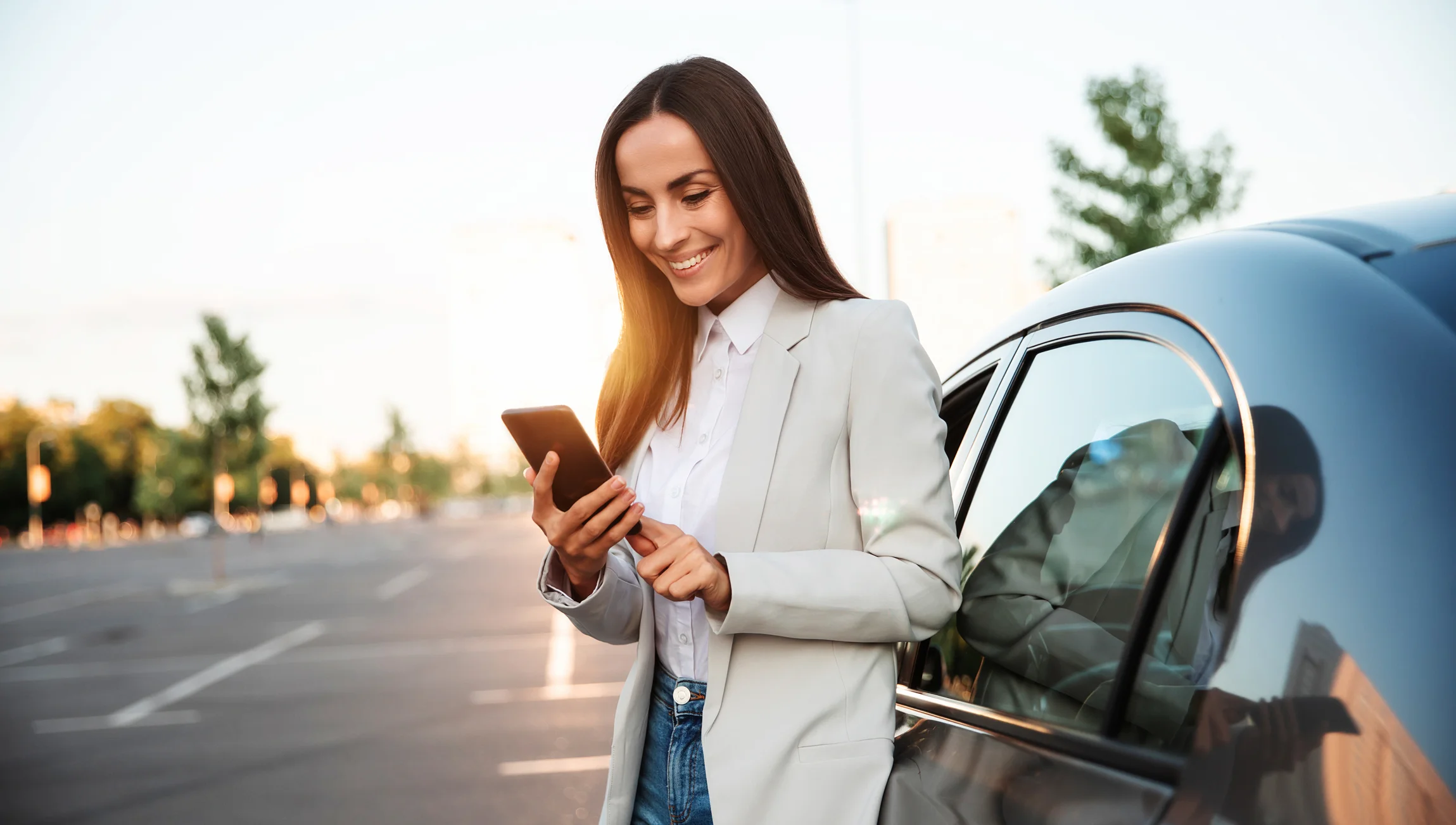 Mujer sonriendo a su teléfono mientras está de pie junto a su coche.